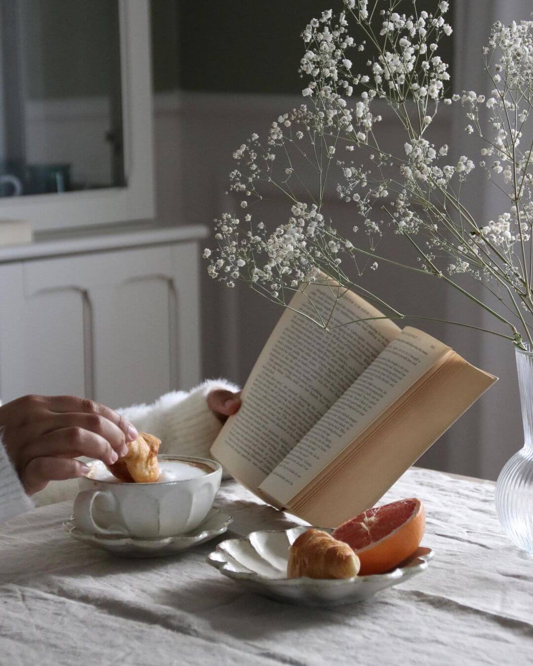 Elegant breakfast setup with Rinka Soup Cup & Plate Set, featuring croissant and grapefruit, accompanied by a book and flowers on a table.