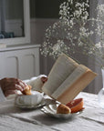Elegant breakfast setup with Rinka Soup Cup & Plate Set, featuring croissant and grapefruit, accompanied by a book and flowers on a table.