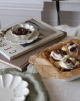Elegant white Rinka plates and bowls displayed with books and pecan-topped pastries, creating a cozy afternoon tea setting.