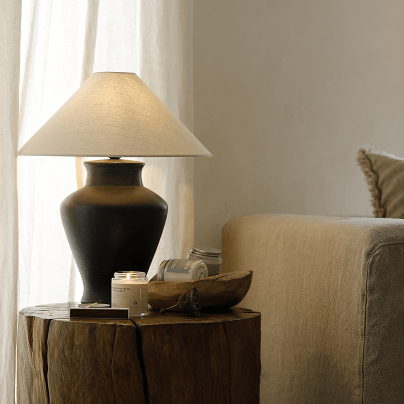 Short Neck Table Lamp with linen shade and clay base on rustic table, emitting warm light, enhancing cozy and clean room ambiance.