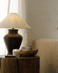 Short Neck Table Lamp with linen shade and clay base on rustic table, emitting warm light, enhancing cozy and clean room ambiance.