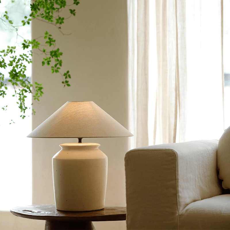 Folding Shoulder Table Lamp with linen shade on wood table beside sofa, adds warm light and decor to room. Adjustable dimming switch.