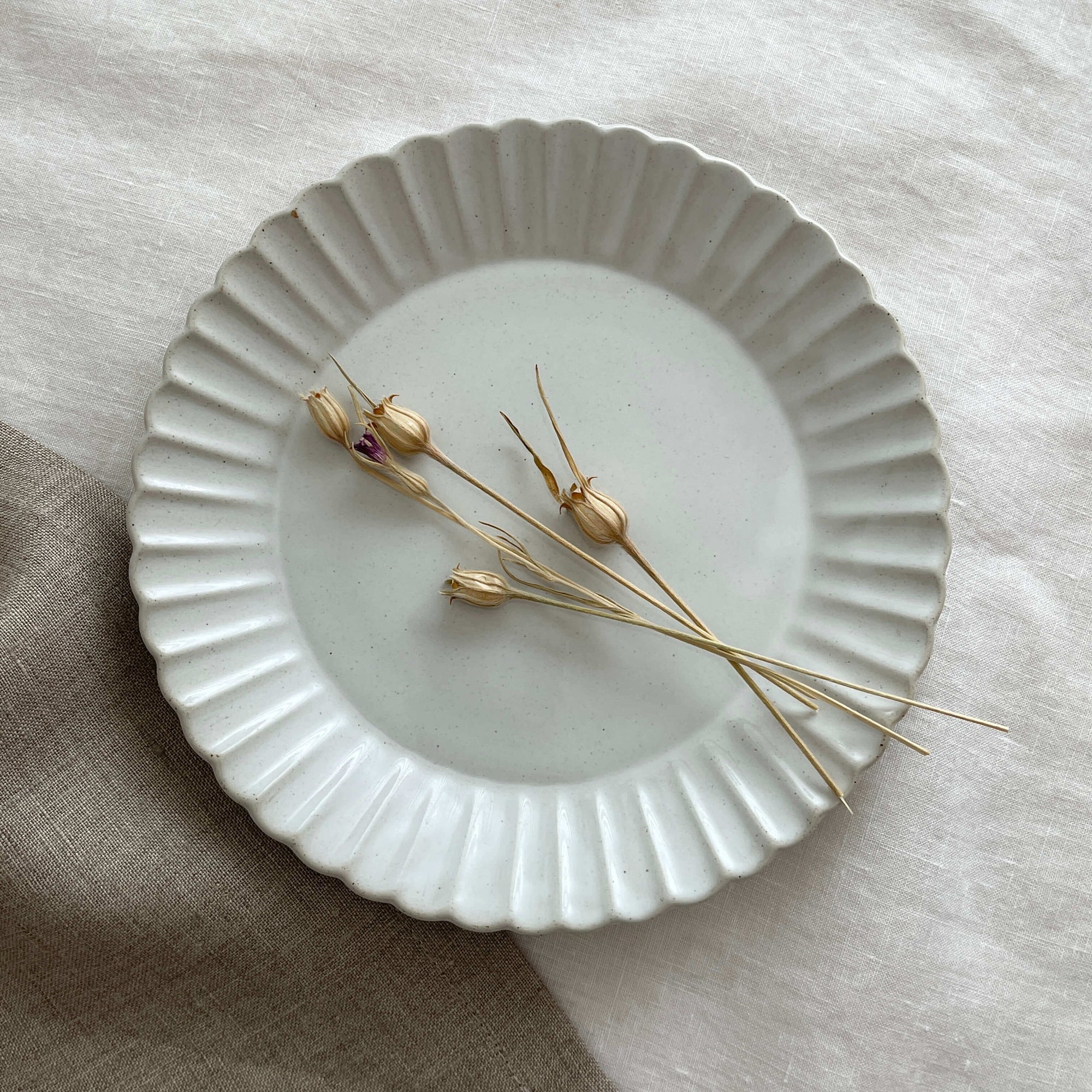 Marumitsu Barbarie plate with petal-like rim and dried flowers on neutral cloth background.