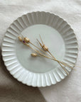 Marumitsu Barbarie plate with petal-like rim and dried flowers on neutral cloth background.