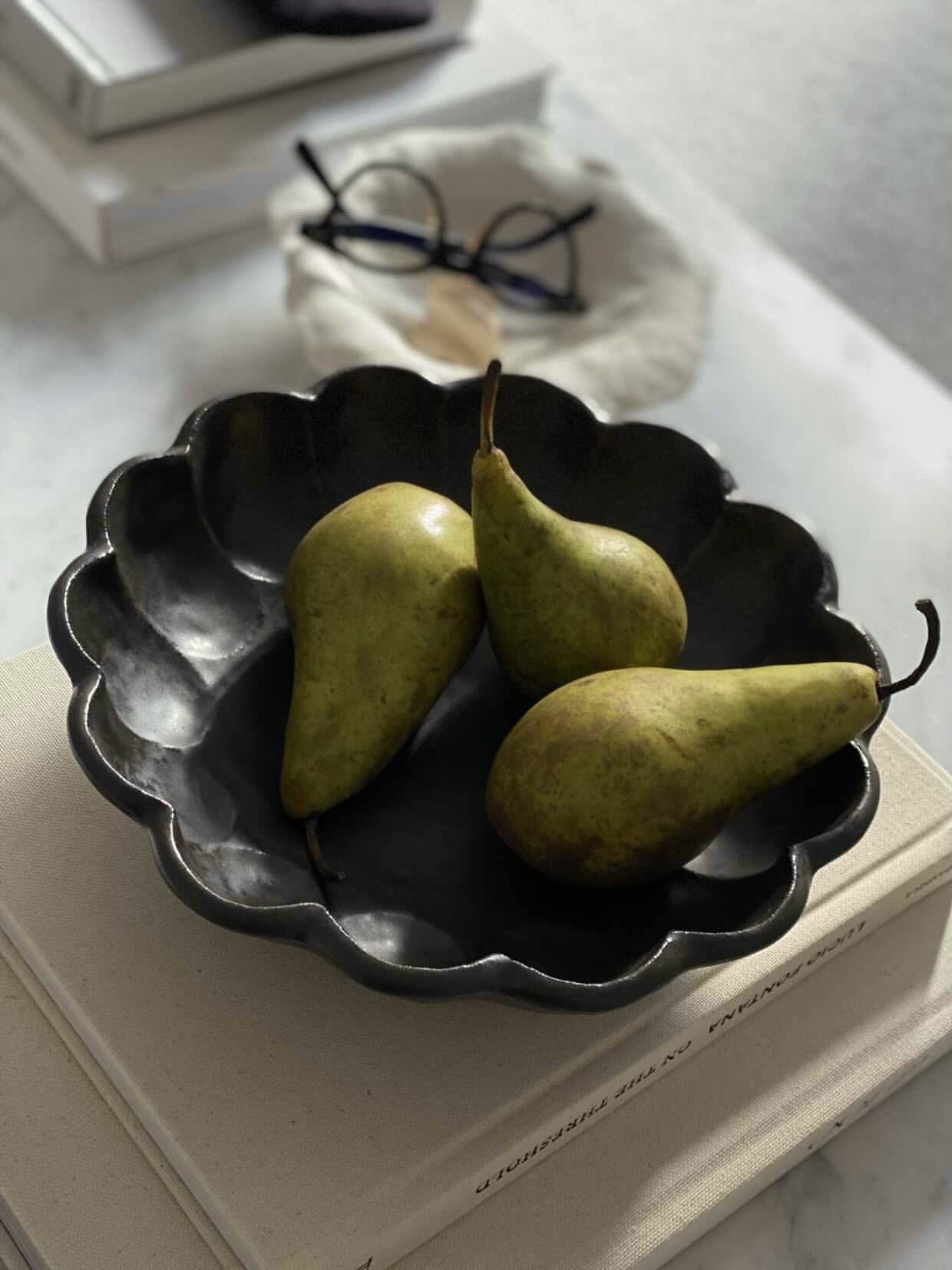 Black Rinka Bowl 24cm with three green pears, showcasing its elegant flower shape on a set table.