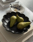 Black Rinka Bowl 24cm with three green pears, showcasing its elegant flower shape on a set table.