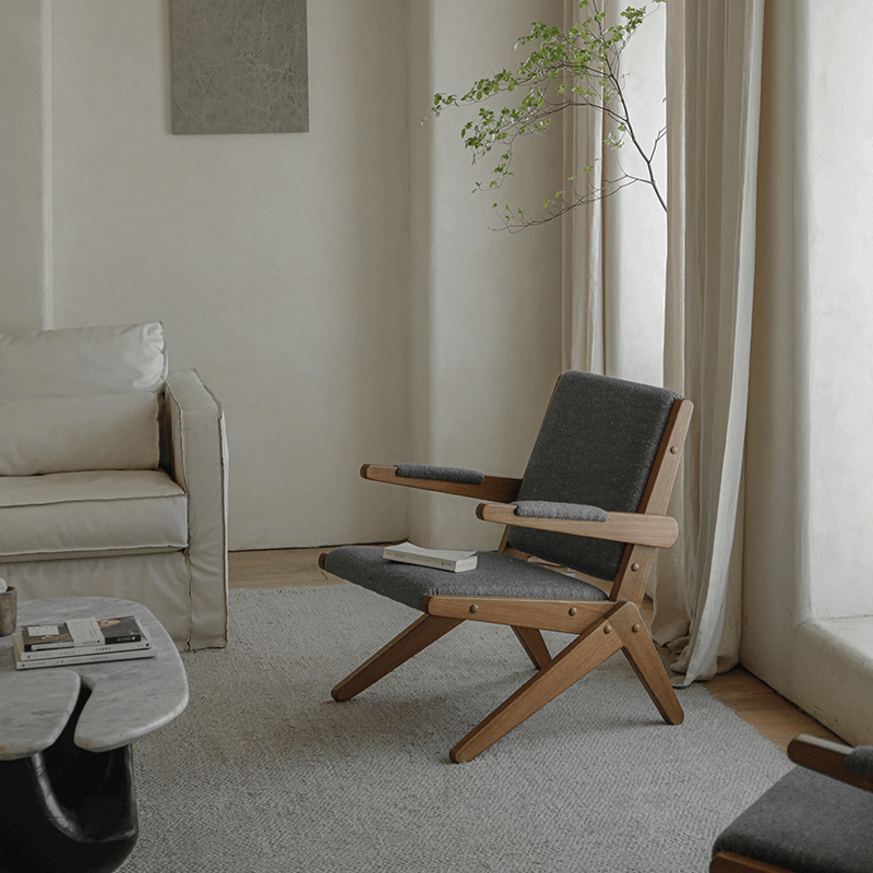 Stylish Scissors Chair with teak wood frame and dark cushions in a modern living room setting.