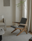Stylish Scissors Chair with teak wood frame and dark cushions in a modern living room setting.