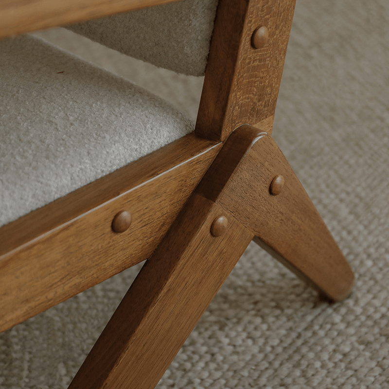 Close-up of the Scissors Chair's teak wood S-shaped frame and armrest detail on a textured carpet background.