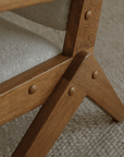 Close-up of the Scissors Chair's teak wood S-shaped frame and armrest detail on a textured carpet background.