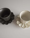 Black and white Rinka mugs from Kaneko Kohyo on flower-shaped saucers, made of delicate porcelain, enhancing table aesthetics.