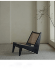 Black rattan Kangaroo Chair with solid wood frame in a minimalist room setting, showcasing unique "Z" shape design and slanted legs.