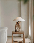 Rustic carved table lamp made from recycled wood on a wooden side table, enhancing a cozy living room atmosphere.