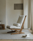 Nakajima George reclining chair in teak wood and rattan, featuring a handmade design with natural linen and foam cushion in a serene room setting.