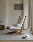 Nakajima George reclining chair in teak wood and rattan, featuring a handmade design with natural linen and foam cushion in a serene room setting.