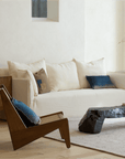 Modern living room featuring a Kangaroo Chair with rattan and wood design, placed beside a rustic coffee table and cream sofa.