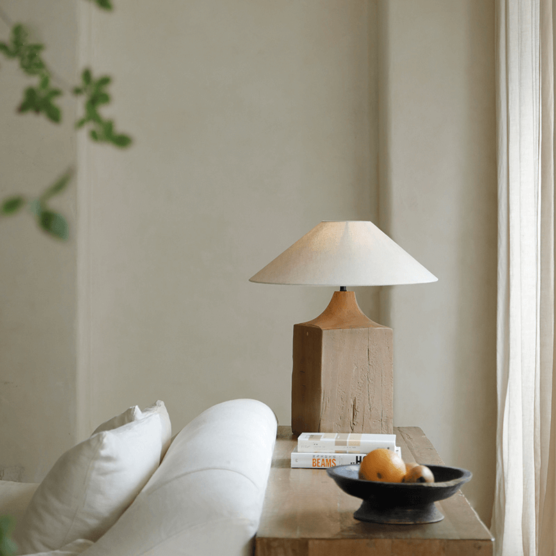 Old wood table lamp with linen lampshade on a wooden desk, creating a natural atmosphere in a cozy living room setting.
