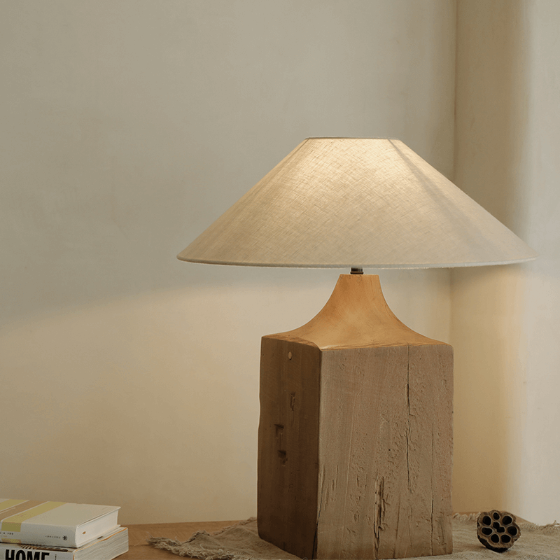 Old wood table lamp with linen shade on wooden surface, hand-polished for a unique look, offering adjustable brightness for a warm atmosphere.