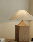 Old wood table lamp with linen shade on wooden surface, hand-polished for a unique look, offering adjustable brightness for a warm atmosphere.