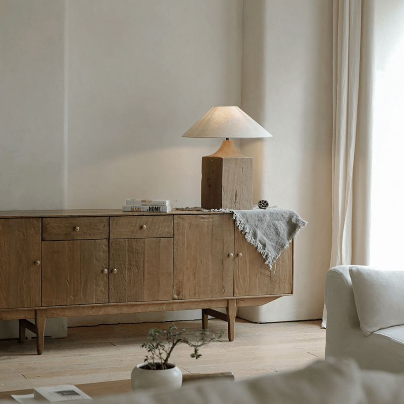 Old wood table lamp with linen shade on sideboard in cozy living room setting, providing warm adjustable lighting.