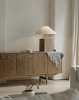 Old wood table lamp with linen shade on sideboard in cozy living room setting, providing warm adjustable lighting.