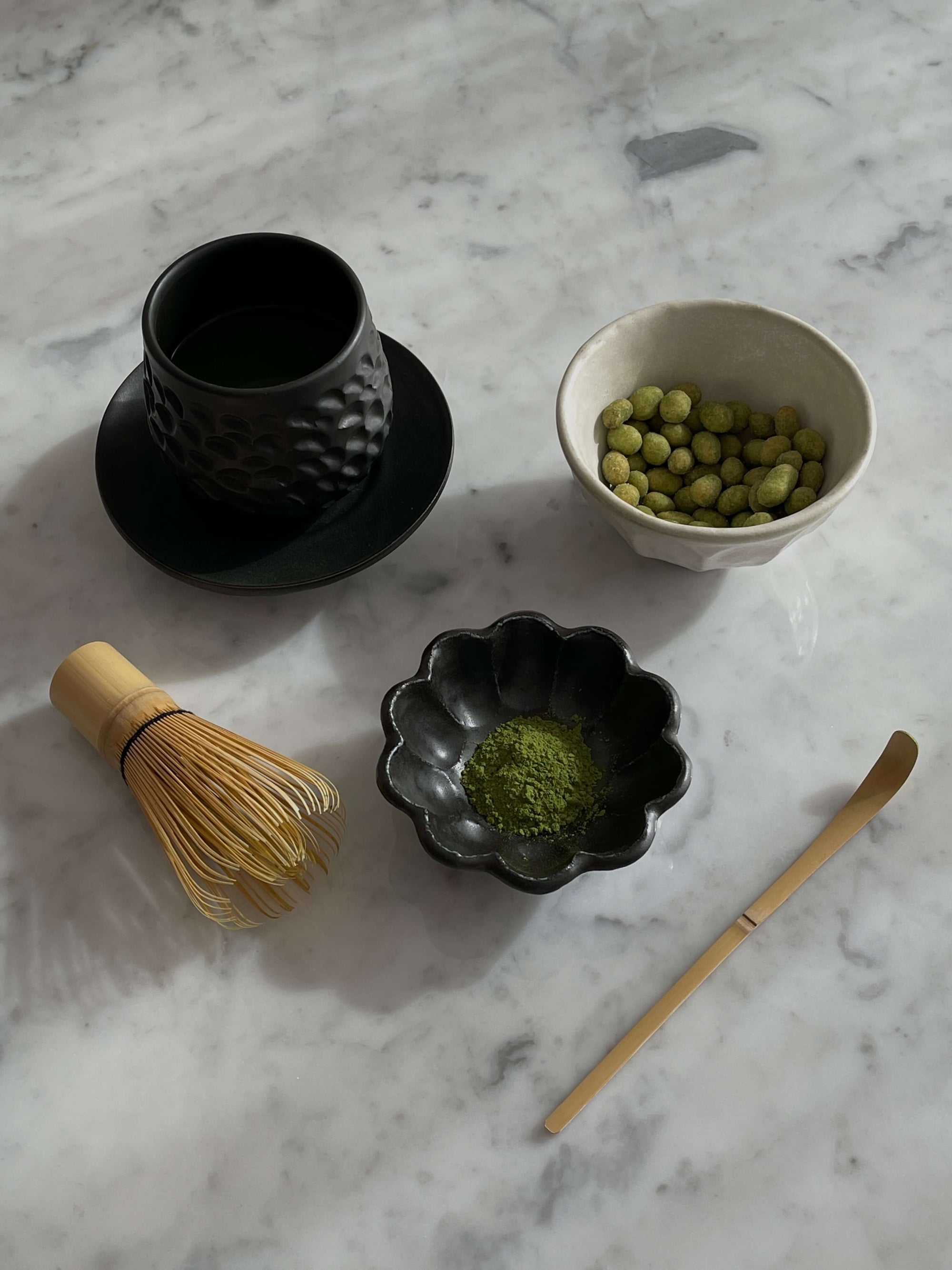 Traditional Japanese tea set with matcha, bowl, whisk, and bamboo scoop on a marble surface.
