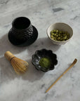 Traditional Japanese tea set with matcha, bowl, whisk, and bamboo scoop on a marble surface.