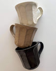 Three stacked Rinka mugs from Kaneko Kohyo's porcelain collection, showcasing flower-inspired design in neutral tones.