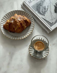 Elegant porcelain plate with croissant and a cup of espresso on a marble table next to art books.