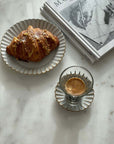Marumitsu Barbarie plate with a croissant and espresso on a marble table, next to art books.