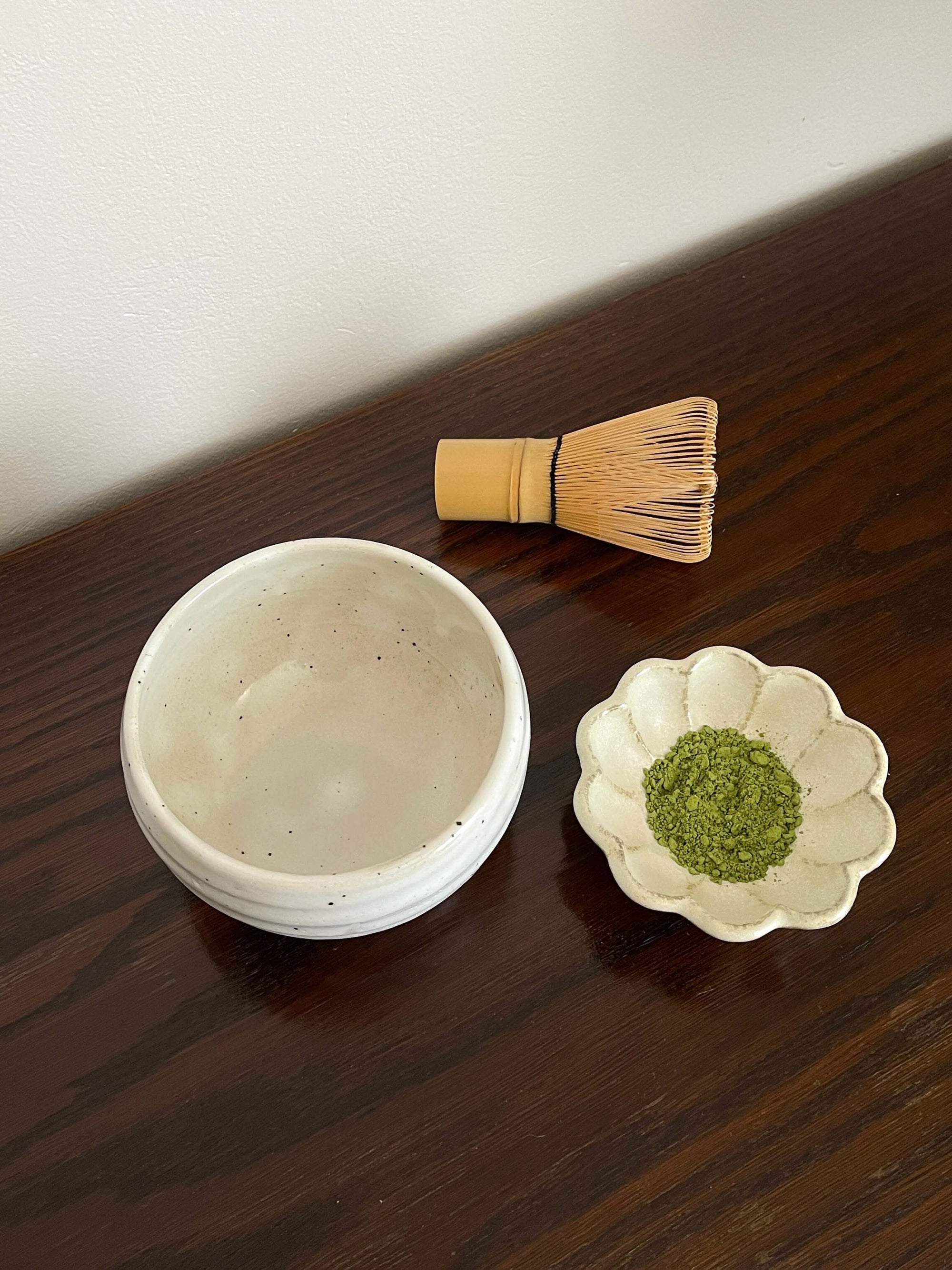 Ivory Matcha Bowl with whisk and matcha powder on a wooden table, showcasing traditional Japanese tea ceremony tools.