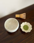 Ivory Matcha Bowl with whisk and matcha powder on a wooden table, showcasing traditional Japanese tea ceremony tools.
