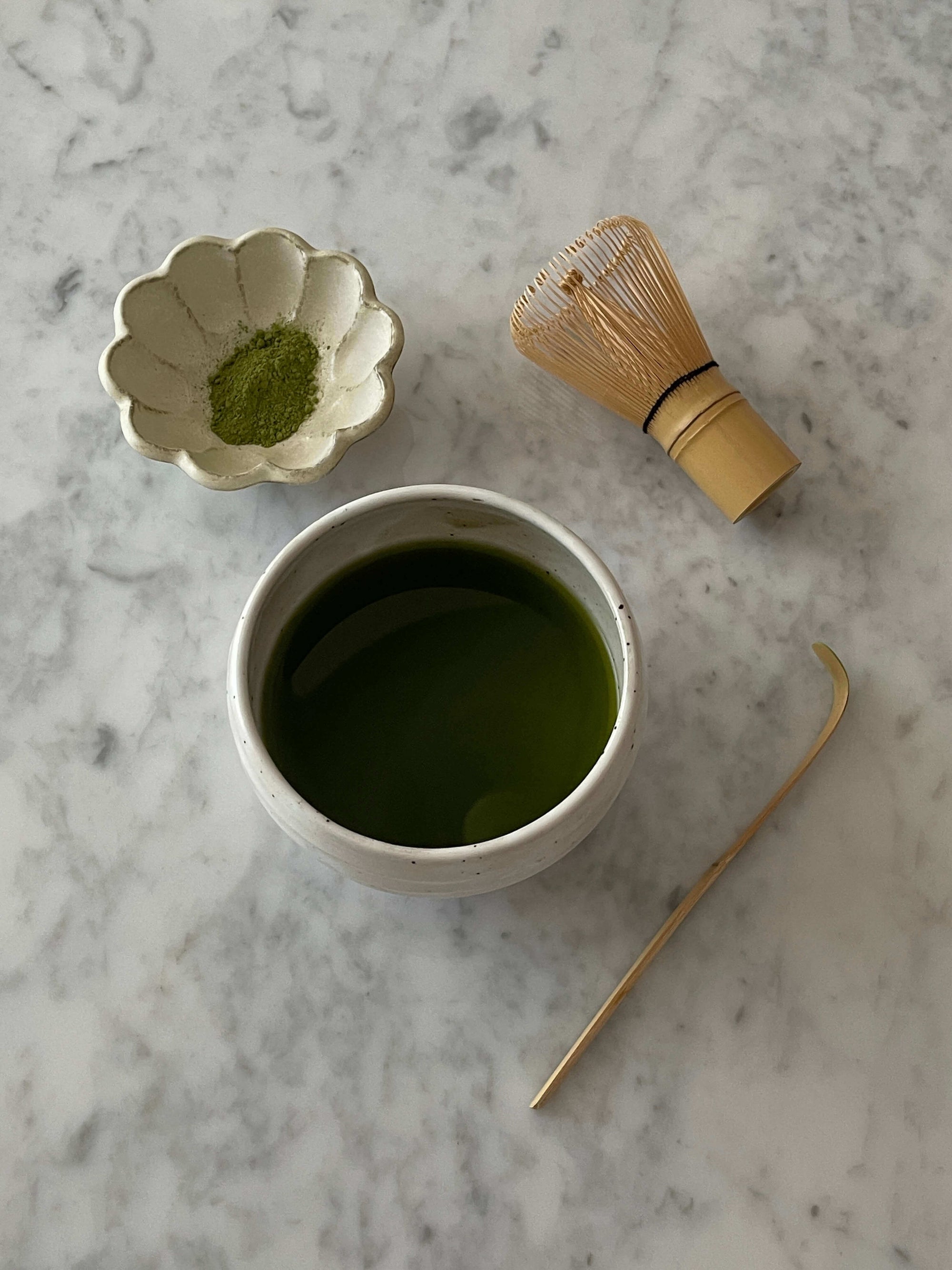 Ivory matcha bowl with whisk and matcha powder on marble surface, exemplifying Japanese matcha culture essentials.