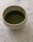 Ivory Matcha Bowl filled with green matcha tea, showcasing its rounded form and calm colors, made of Mino ware porcelain.