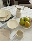 Yoshida Pottery Collection on marble table with plates, bowl, cup, vase, and pears in a tray, showcasing elegant ceramic craftsmanship.