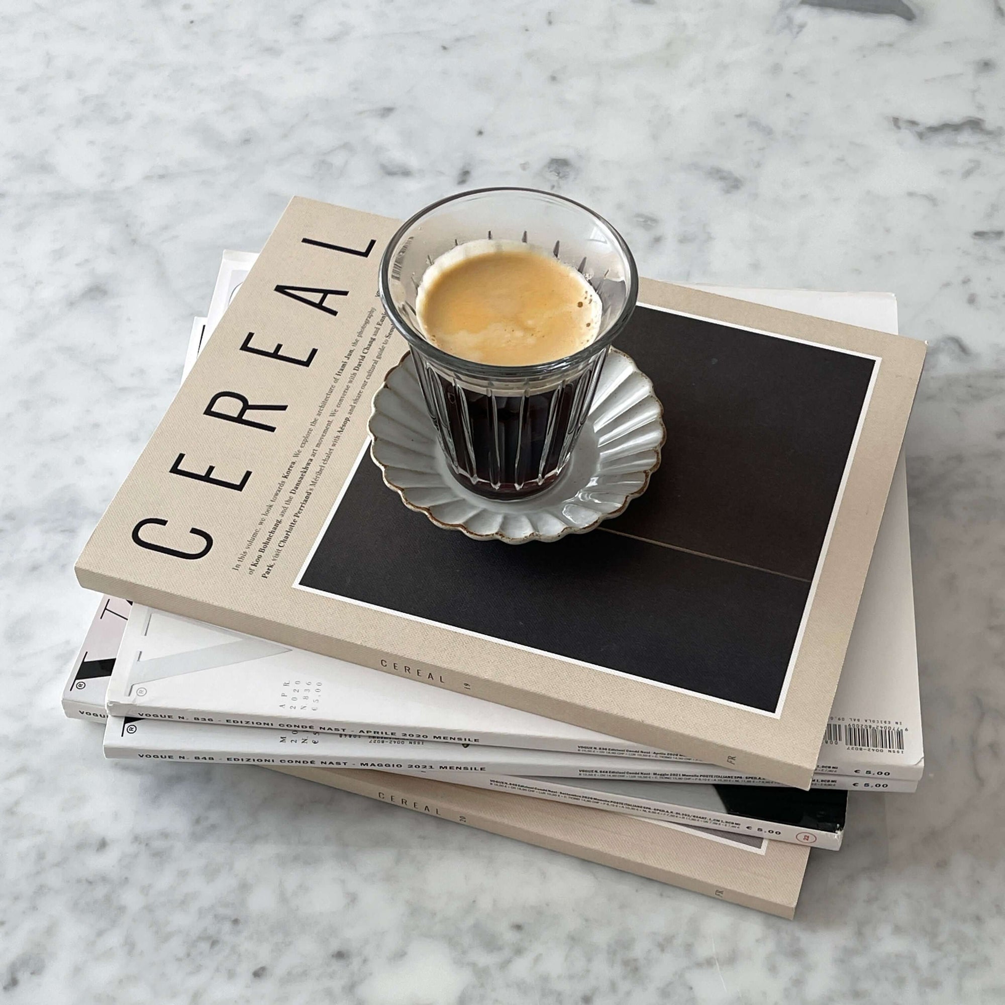 Espresso served on a fluted saucer atop Cereal magazine stack on marble surface