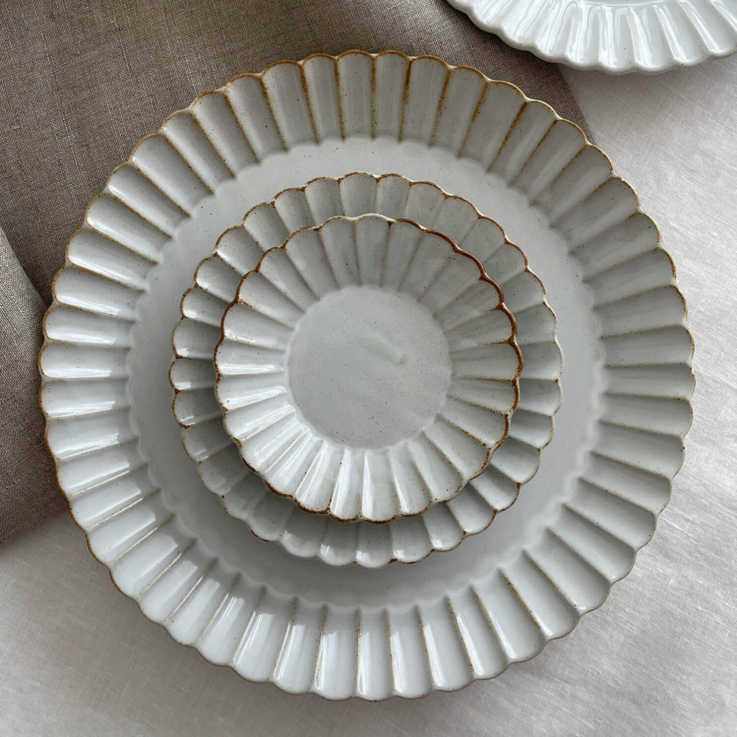 Elegant Marumitsu Barbarie plates with petal-like rim relief, stacked on a neutral fabric background. Perfect for sophisticated dining.