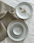 Elegant Marumitsu Barbarie plates with petal-like rims displayed on fabric, showcasing sophisticated design and pottery craftsmanship.