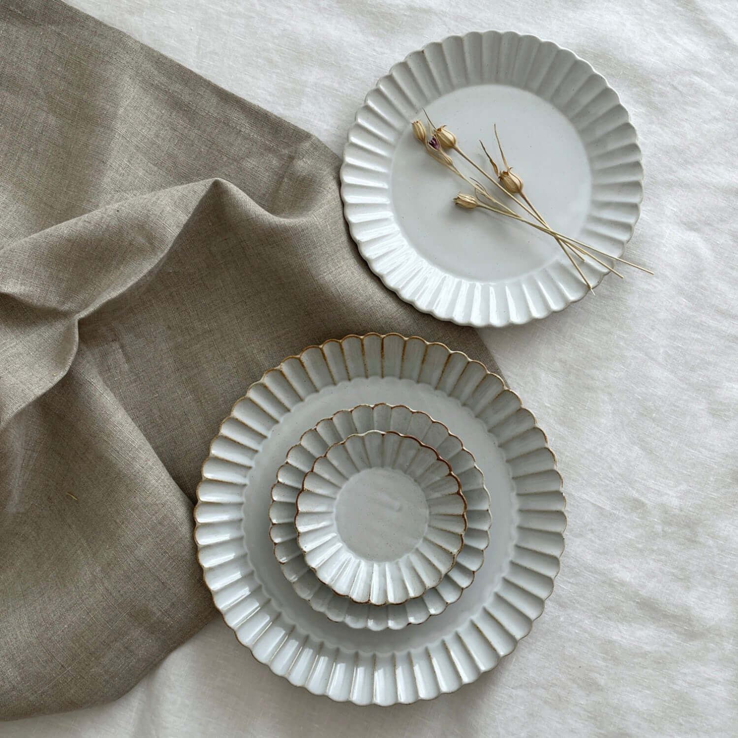 Elegant Marumitsu Barbarie plates with petal-like rims displayed on fabric, showcasing sophisticated design and pottery craftsmanship.