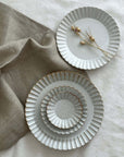 Elegant Marumitsu Barbarie plates with petal-like rims displayed on fabric, showcasing sophisticated design and pottery craftsmanship.