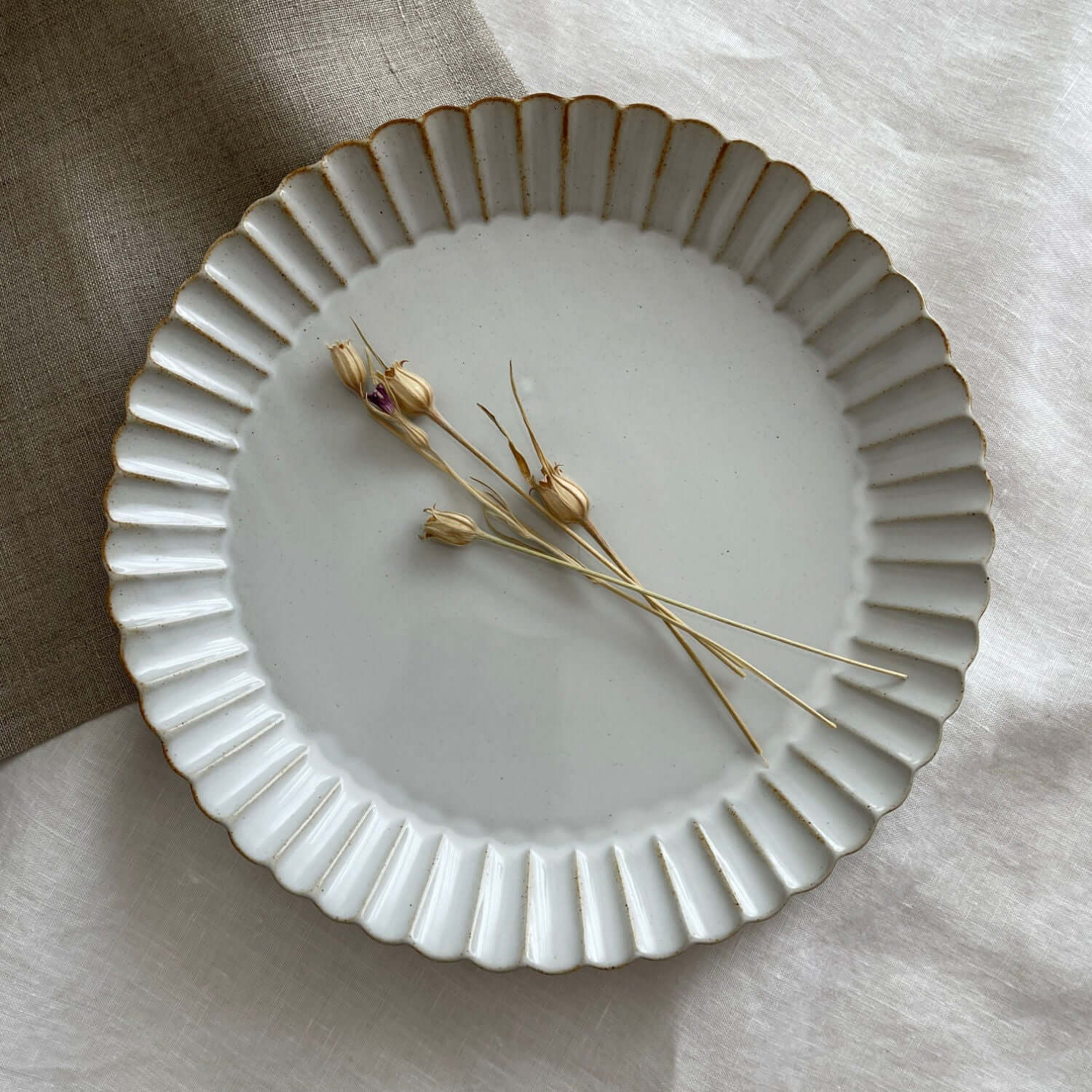 Marumitsu Barbarie plate with petal-like rim and dried flowers on a fabric background