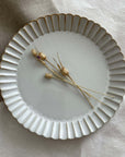 Marumitsu Barbarie plate with petal-like rim and dried flowers on a fabric background