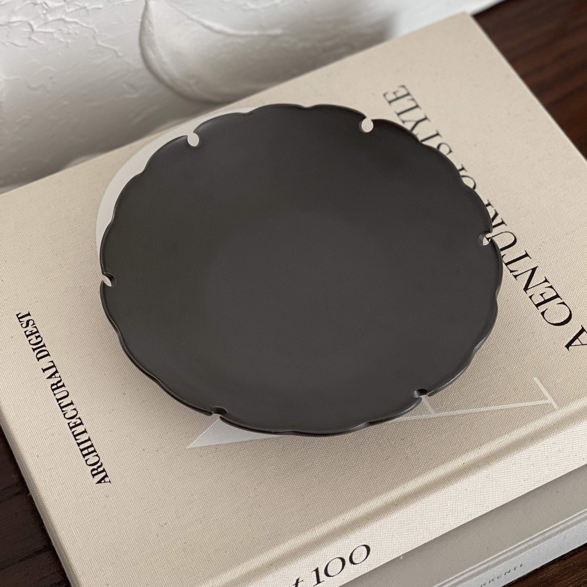 Yukiwa Plate by Yoshida Pottery displayed on a book, showcasing elegant nature-inspired design in dark ceramic.