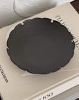 Yukiwa Plate by Yoshida Pottery displayed on a book, showcasing elegant nature-inspired design in dark ceramic.