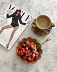 Rustic bowl with fresh berries and cream, paired with a floral-shaped coffee cup and a fashion magazine on a marble table.