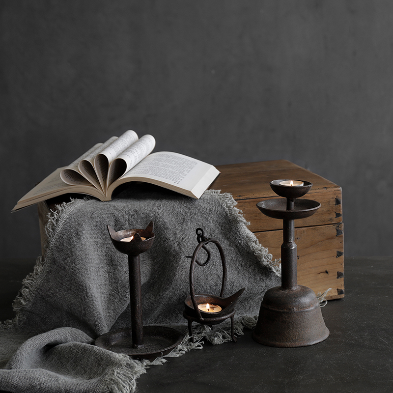Antique Aimu table candle holder set with distressed details, displayed beside an open book on a rustic wooden box.
