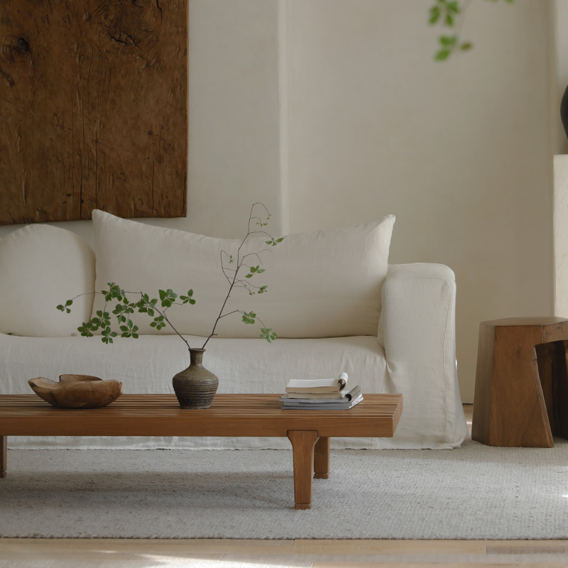 Minimalist living room with modern fence coffee table, natural wood finish, decorative vase and books, cozy white sofa in the background.