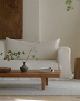 Minimalist living room with modern fence coffee table, natural wood finish, decorative vase and books, cozy white sofa in the background.