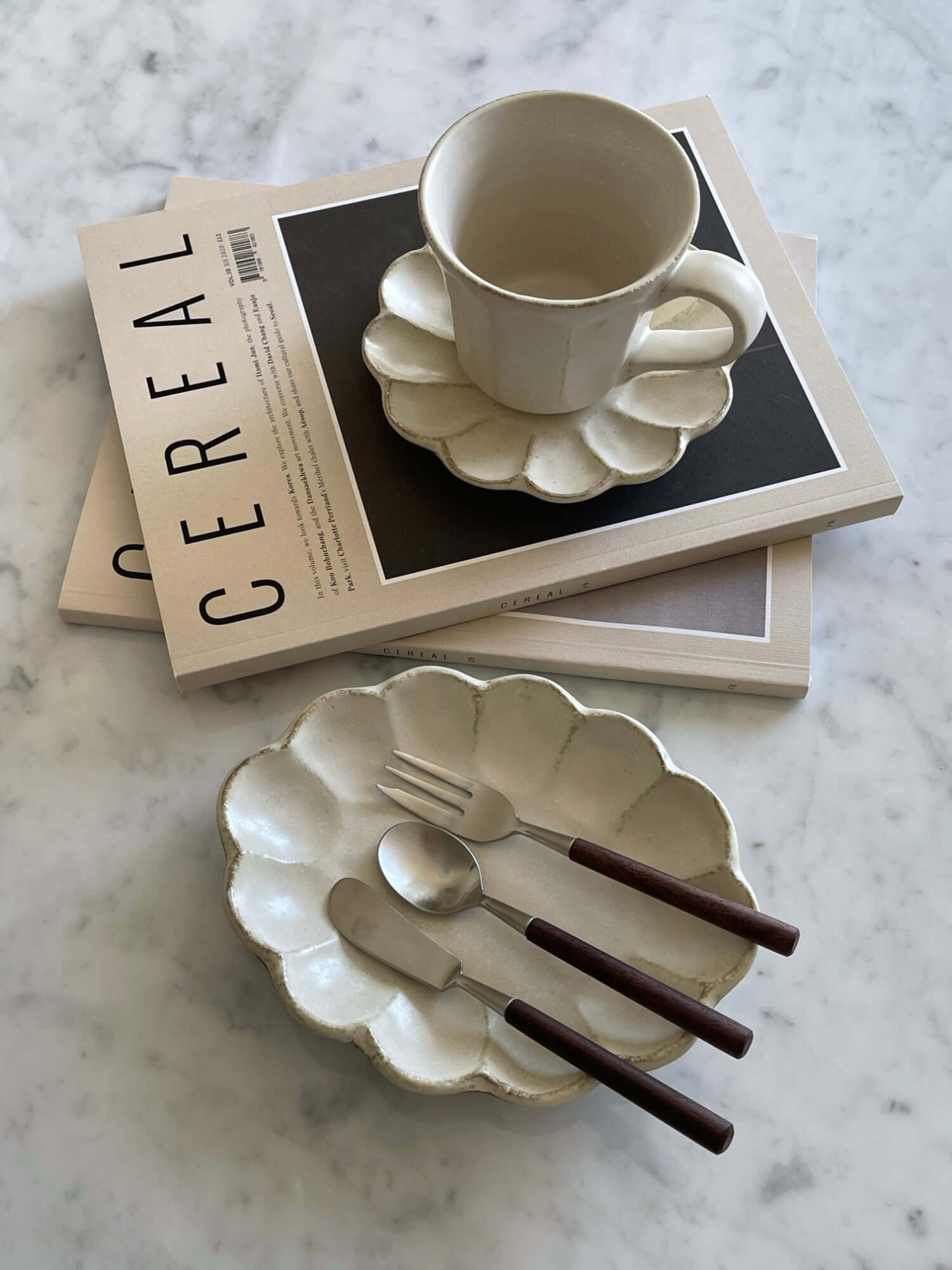 Porcelain flower-shaped Rinka oval plate and cup from Kaneko Kohyo's collection, styled with cutlery on a marble surface.