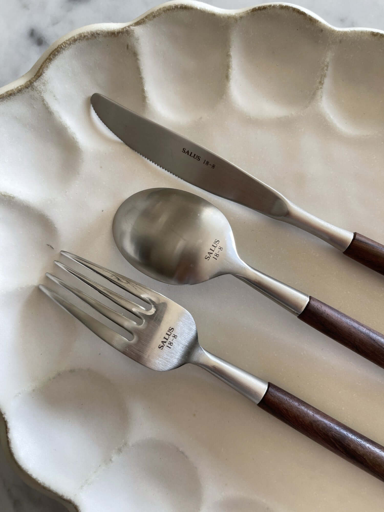 Elegant Rosewood cutlery set on white plate, featuring a knife, fork, and spoon with unique wooden handles.